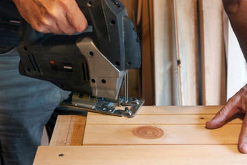 A carpenter cuts off the edge of a board with an electric jigsaw machine in a carpentry workshop Close up hand with a jigsaw. Joinery production and concept