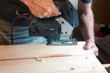 A carpenter saws a board with an electric jigsaw machine in a carpentry workshop. Close up hand with a jigsaw. Joinery production and concept.