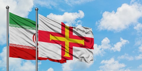 Iran and Guernsey flag waving in the wind against white cloudy blue sky together. Diplomacy concept, international relations.