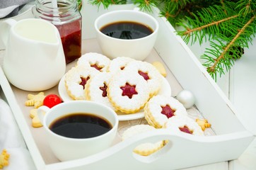 Christmas Linzer cookies filled with strawberry jam on a white plate on a tray with two cups of coffee. Morning Christmas, Christmas breakfast.