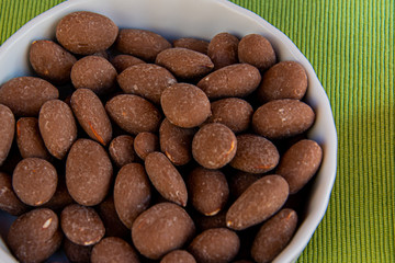 Almond or prunus dulcis covered with chocolate on white tray.