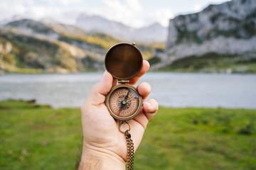 A hand holds a compass in a mountain and lake landscape