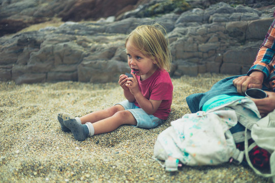 Toddler on beach with mother eating chocolate