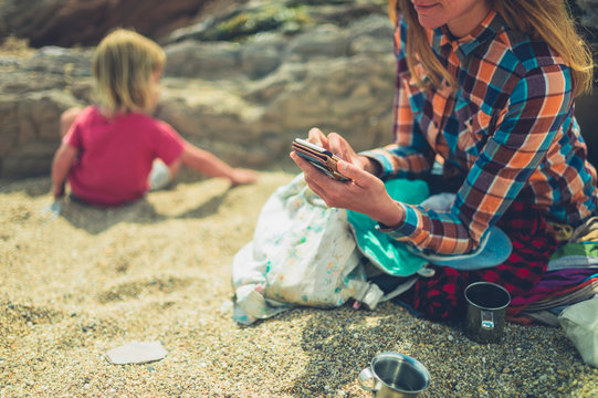 Mother with toddler using smartphone on the beach