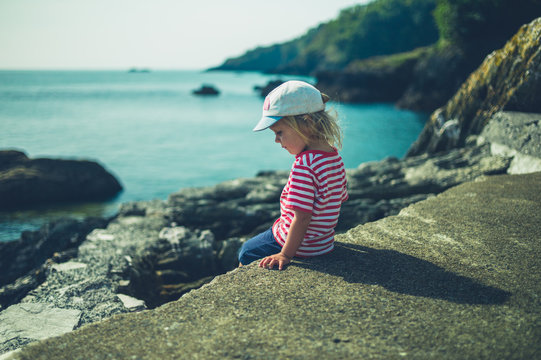 Little toddler sitting on a rock by the sea