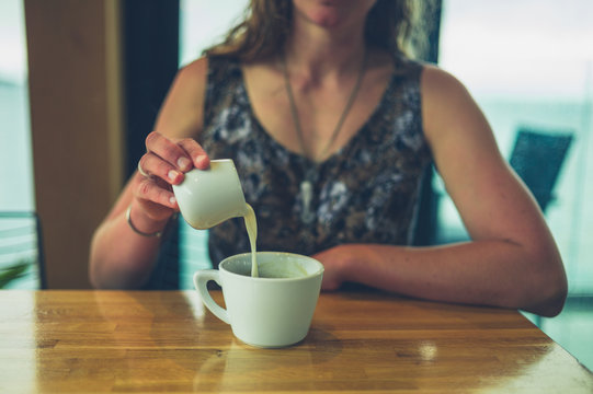 Young woman pouring cream in her coffee