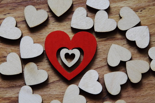 Combined heart made of wood painted red and wooden hearts of natural color on wooden surface. Symbolic concept love, relationship. Congratulatory concept for birthday, Mother's Day, Valentine's Day.