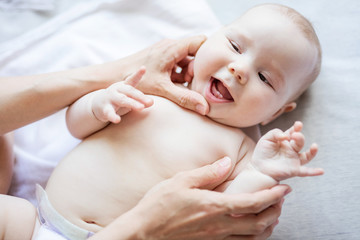Cheerful baby girl lying on bed while mother looking at her first teeth