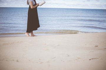 Female standing on the beach shore near the water bare feet while reading the bible
