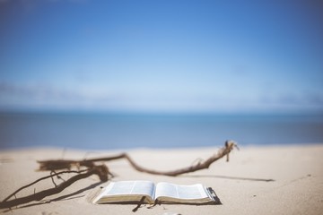 Closeup shot of an open bible on a sandy shore with a blurred sea in the background