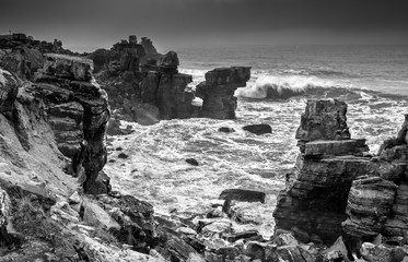 A huge ocean waves breaking on the coastal cliffs in at the cloudy stormy day. Breathtaking romantic seascape of ocean coastline. Bw photo. Peniche, Portugal.
