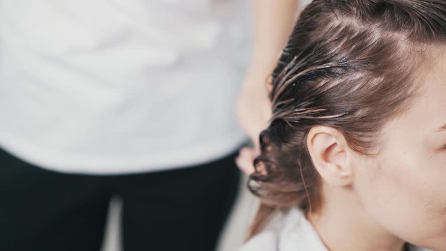 Close Up Of Hairdresser Hands Applying Hair Mask On Hair Of Young Woman