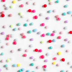 Texture of small colorful textile fluffy pompons on a white background. Flat lay. Creative.
