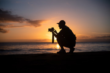 The silhouette of a male hobbyist photographer taking photos of a beautiful colorful sunset on the...