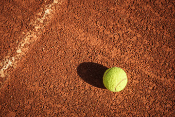 Yellow tennis ball laying on a typical red clay ground court
