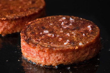 Plant based vegetarian burger patties with rock salt being cooked on flat black iron grill.
