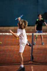 8 years old boy playing tennis with his 12 years old brother, finishing a smash movement © Nicolas Viard