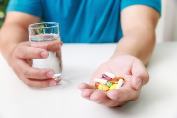 Close up of Colorful pills, capsule medicines and glass of water in man's hands. Medical and Health care or illness concept.