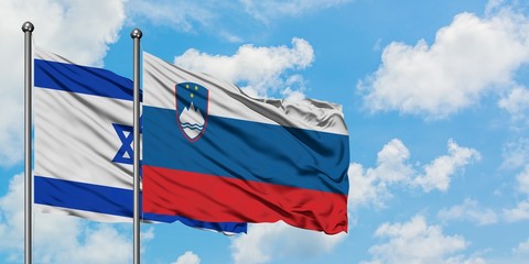 Israel and Slovenia flag waving in the wind against white cloudy blue sky together. Diplomacy...