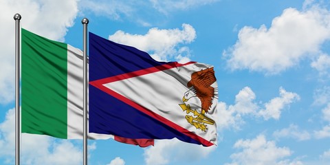 Italy and American Samoa flag waving in the wind against white cloudy blue sky together. Diplomacy...