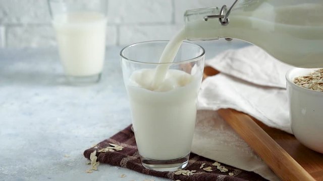 Cook pouring homemade oat milk in glass . On light stone background. Alternative food