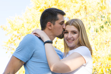 Fototapeta premium Tan Husband kissing with tenderness and love the forehead of his Blond wife. Heterosexual couple embracing and hug on a intimacy date in fall. Happy couple in harmony.