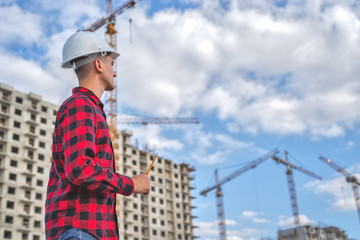 civil engineer in a white helmet and plaid shirt on the background of a house under construction