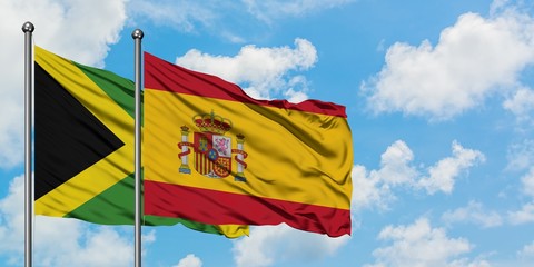 Jamaica and Spain flag waving in the wind against white cloudy blue sky together. Diplomacy...