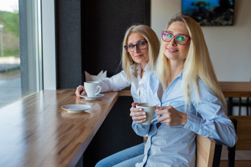 eautiful blonde with glasses and her elderly mother are sitting in a cafe and drinking coffee. Mothers Day. Beautiful aged woman and her adult daughter are smiling and chatting. Related resemblance.