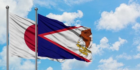 Japan and American Samoa flag waving in the wind against white cloudy blue sky together. Diplomacy...