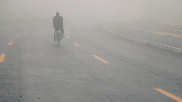 Mystical fog in the city. A man cyclist rides on the road in heavy fog. Highway in heavy fog. Road signs on the highway. Poor visibility on the highway. The mysterious road