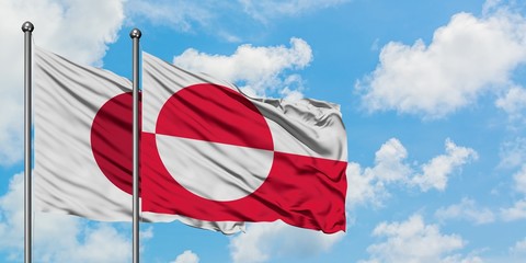 Japan and Greenland flag waving in the wind against white cloudy blue sky together. Diplomacy...
