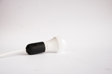 The white economical light bulb in a black cartridge lies on a table on a white background.