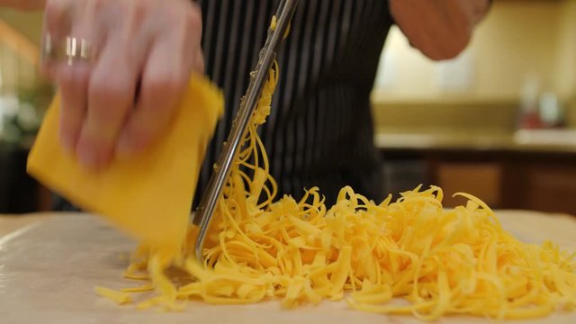 Chef grating cheddar cheese. Female using hand held metal grater to shred yellow cheese.