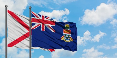 Jersey and Cayman Islands flag waving in the wind against white cloudy blue sky together. Diplomacy concept, international relations.