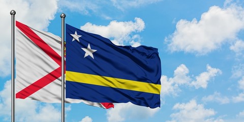 Jersey and Curacao flag waving in the wind against white cloudy blue sky together. Diplomacy concept, international relations.