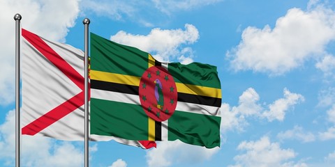Jersey and Dominica flag waving in the wind against white cloudy blue sky together. Diplomacy concept, international relations.