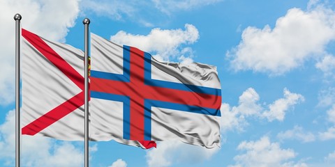 Jersey and Faroe Islands flag waving in the wind against white cloudy blue sky together. Diplomacy...