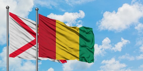 Jersey and Guinea flag waving in the wind against white cloudy blue sky together. Diplomacy concept, international relations.