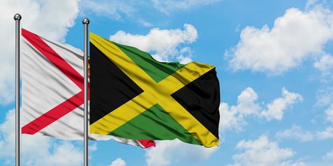 Jersey and Jamaica flag waving in the wind against white cloudy blue sky together. Diplomacy concept, international relations.