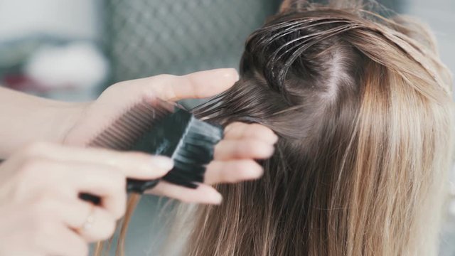 Close up of hairdresser hands applying hair mask on hair of young woman