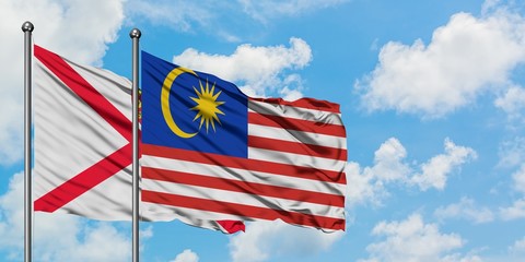 Jersey and Malaysia flag waving in the wind against white cloudy blue sky together. Diplomacy concept, international relations.