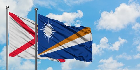 Jersey and Marshall Islands flag waving in the wind against white cloudy blue sky together....