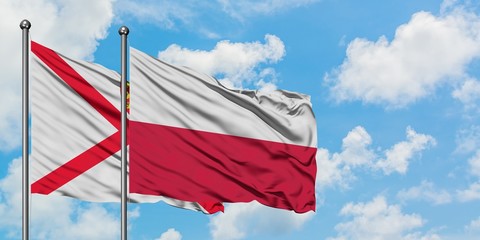 Jersey and Poland flag waving in the wind against white cloudy blue sky together. Diplomacy concept, international relations.