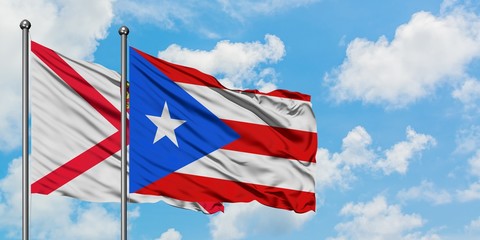 Jersey and Puerto Rico flag waving in the wind against white cloudy blue sky together. Diplomacy concept, international relations.