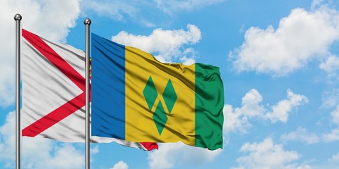Jersey and Saint Vincent And The Grenadines flag waving in the wind against white cloudy blue sky...