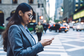 Busy delighted female in eyeglasses typing on mobile