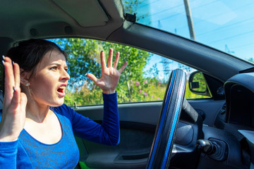 Angry woman driving a car. The girl with an expression of displeasure is actively gesticulating behind the wheel of the car. Car insurance concept