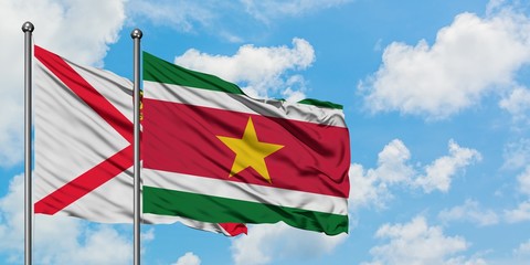 Jersey and Suriname flag waving in the wind against white cloudy blue sky together. Diplomacy concept, international relations.