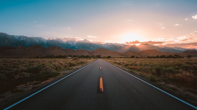 Straight road in the middle of the desert with magnificent mountains and the sunset
